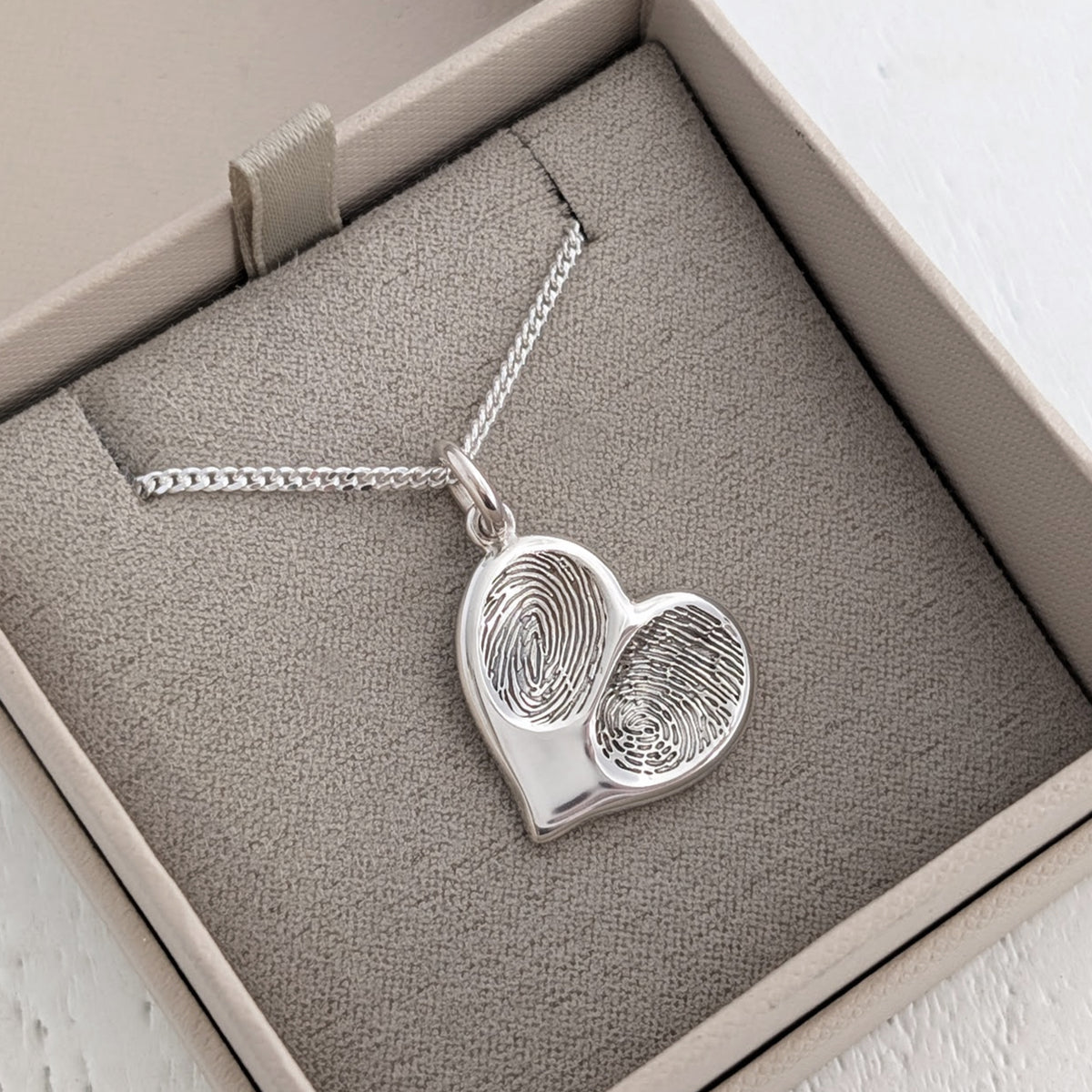 Handmade double fingerprint necklace in sterling silver, showcasing unique engraved fingerprints on a polished heart charm suspended from a silver chain.