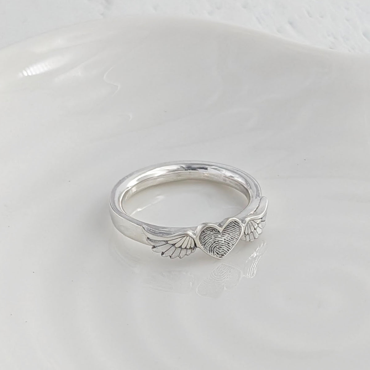 Personalised fingerprint angel wing ring, handmade in silver with a heart engraved with your loved one’s unique fingerprint.