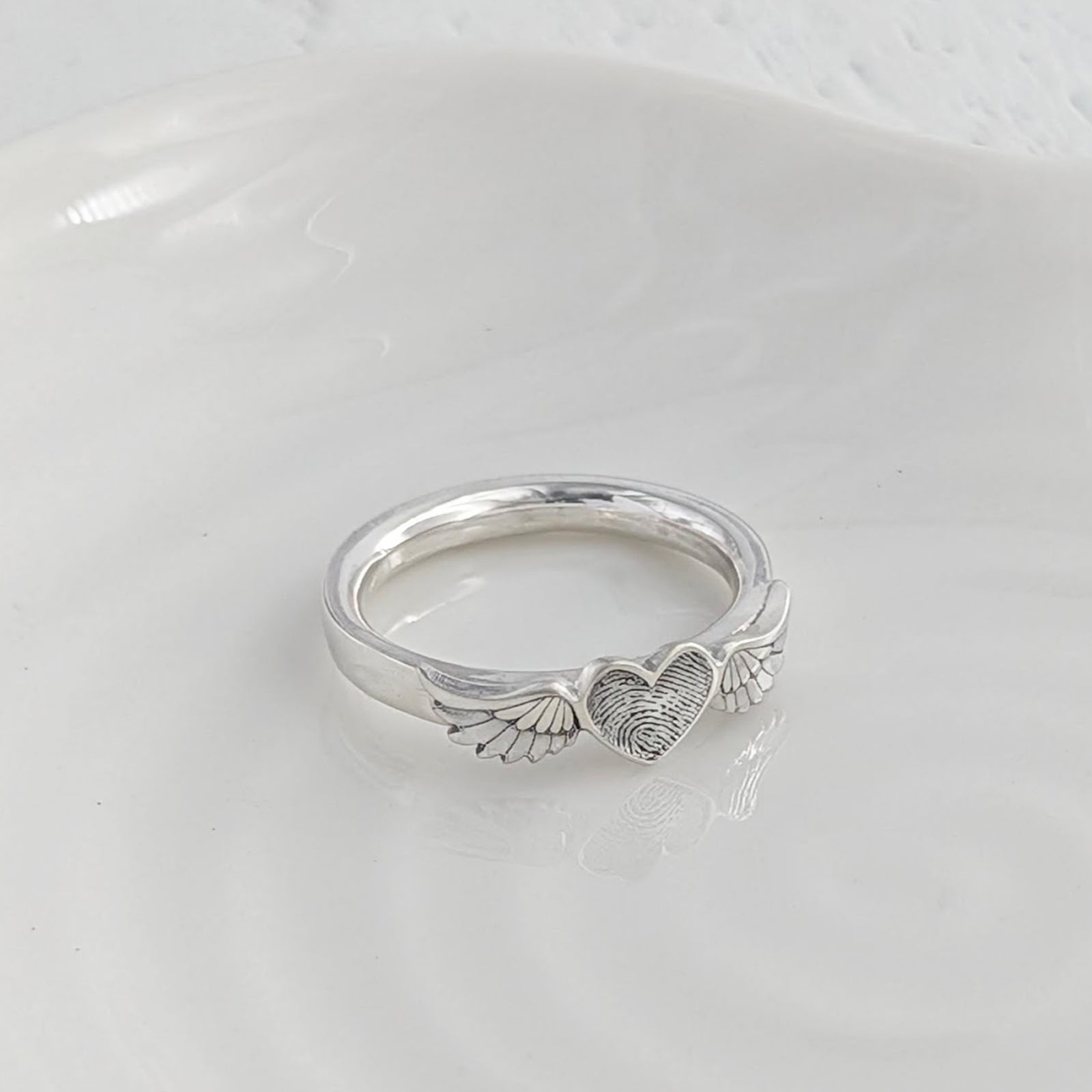 Personalised fingerprint angel wing ring, handmade in silver with a heart engraved with your loved one’s unique fingerprint.