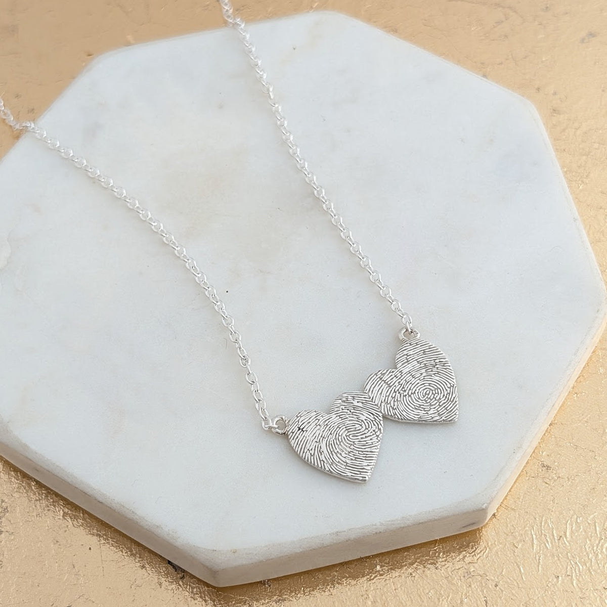 Heart to Heart Fingerprint Necklace in Silver or Gold – Two intertwined heart charms engraved with real fingerprints, creating a beautiful symbol of love and connection. Handmade in sterling silver or solid gold.
