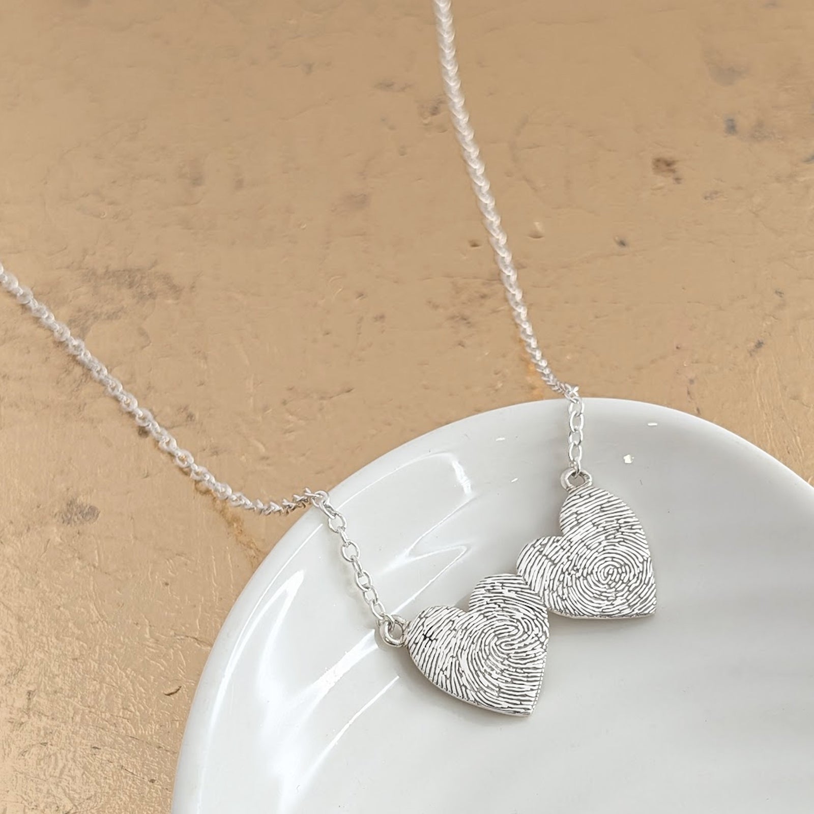 Fingerprint Heart to Heart Necklace – A beautiful personalised necklace featuring two connected heart pendants engraved with real fingerprints. Handmade in sterling silver or solid gold, symbolising the unbreakable bond between two loved ones and keeping treasured memories close every day.