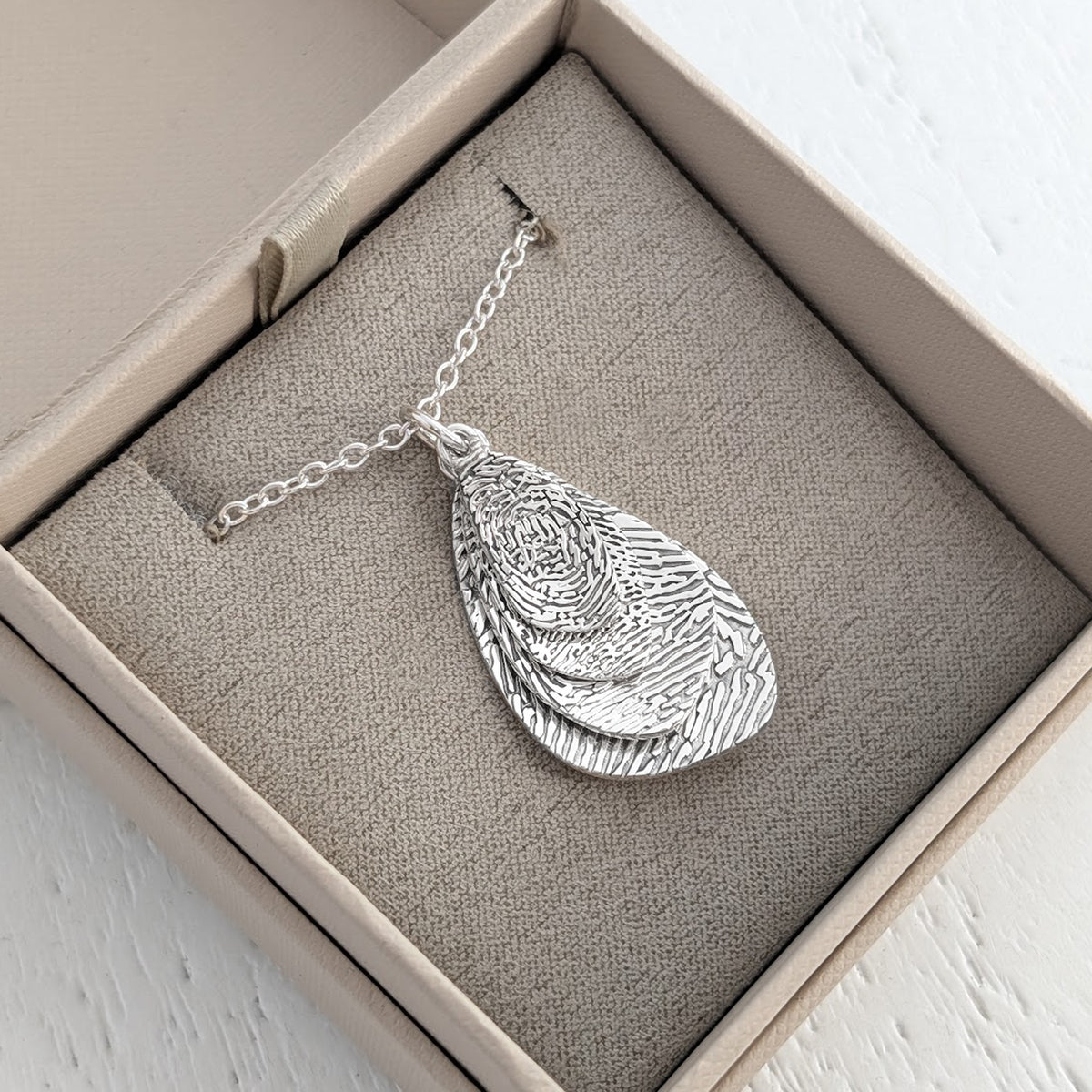 Personalised Organic Fingerprint Pendant Necklace – Elegant layered droplet charms featuring the intricate detail of a genuine fingerprint. Handcrafted in sterling silver or gold as a contemporary memorial or sentimental jewellery gift.
