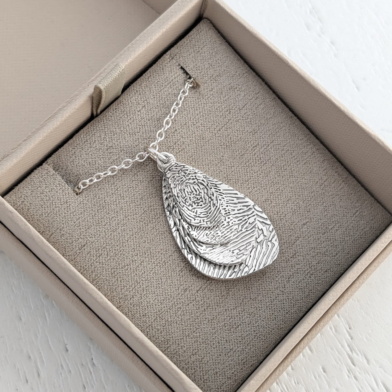 Personalised Organic Fingerprint Pendant Necklace – Elegant layered droplet charms featuring the intricate detail of a genuine fingerprint. Handcrafted in sterling silver or gold as a contemporary memorial or sentimental jewellery gift.