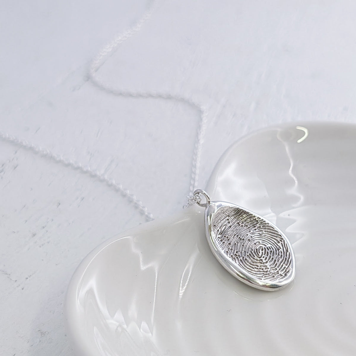 Bespoke Organic Fingerprint Jewellery necklace featuring a real fingerprint engraved into a smooth organic pendant. Available in sterling silver and solid gold, this elegant personalised necklace makes a thoughtful memorial or family keepsake gift.