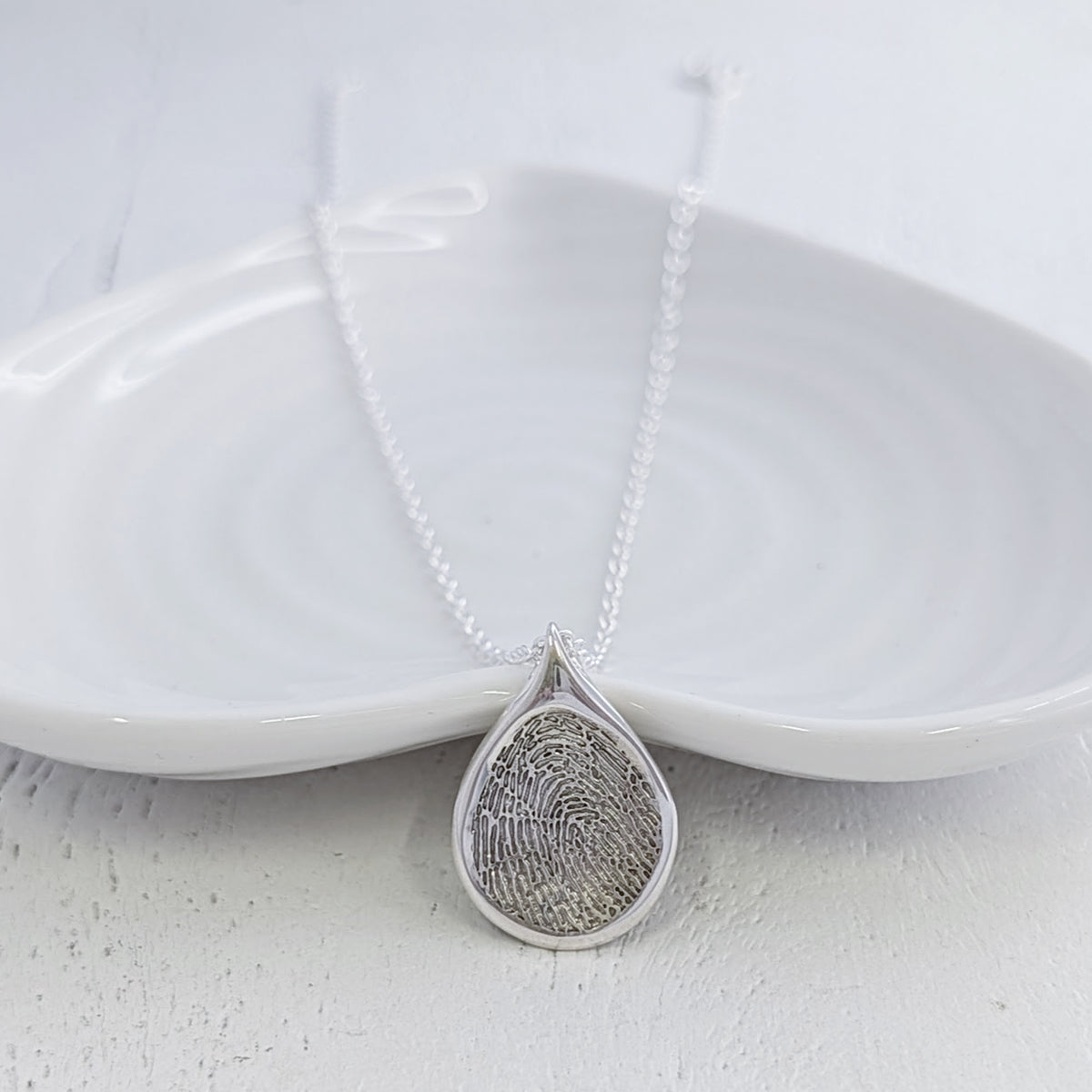 Personalised Droplet Fingerprint Necklace handcrafted in sterling silver or solid gold. Featuring your loved one’s real fingerprint engraved within a contemporary teardrop design, creating a meaningful keepsake or memorial jewellery piece.