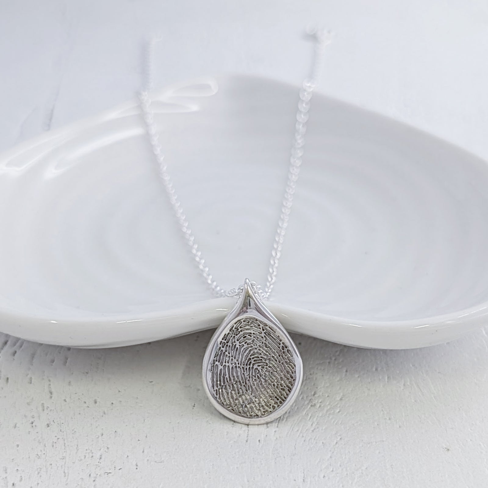 Personalised Droplet Fingerprint Necklace handcrafted in sterling silver or solid gold. Featuring your loved one’s real fingerprint engraved within a contemporary teardrop design, creating a meaningful keepsake or memorial jewellery piece.