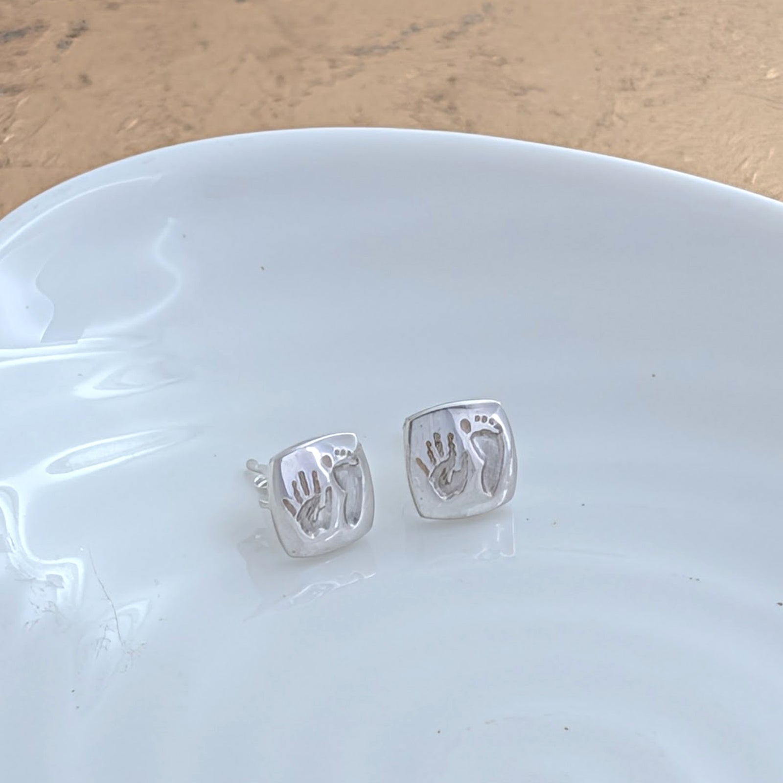 Handmade baby handprint and footprint stud earrings with softly rounded cushion-shaped faces, available in sterling silver and solid gold for a meaningful everyday reminder.