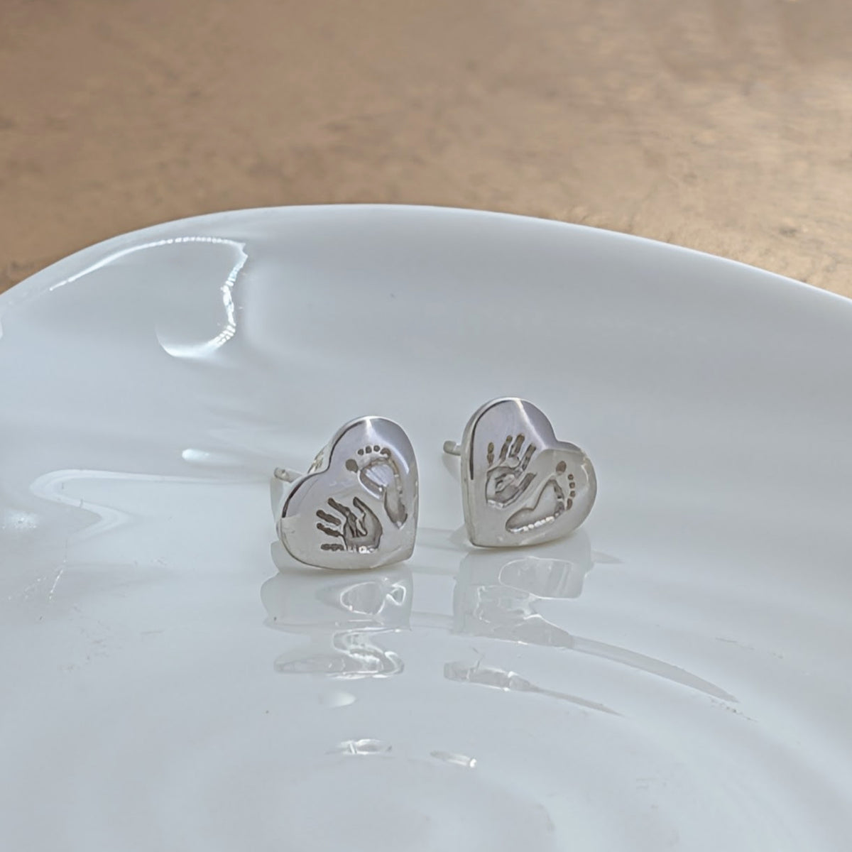 Personalised handprint and footprint earrings crafted in sterling silver, featuring real baby prints engraved onto heart-shaped studs. Handmade keepsake jewellery from Shropshire.