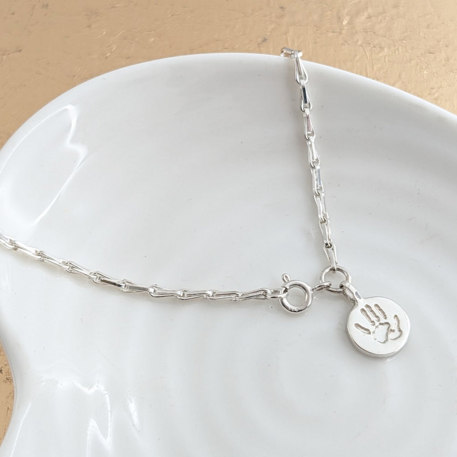 Silver bracelet with a hand-shaped charm on a white dish
