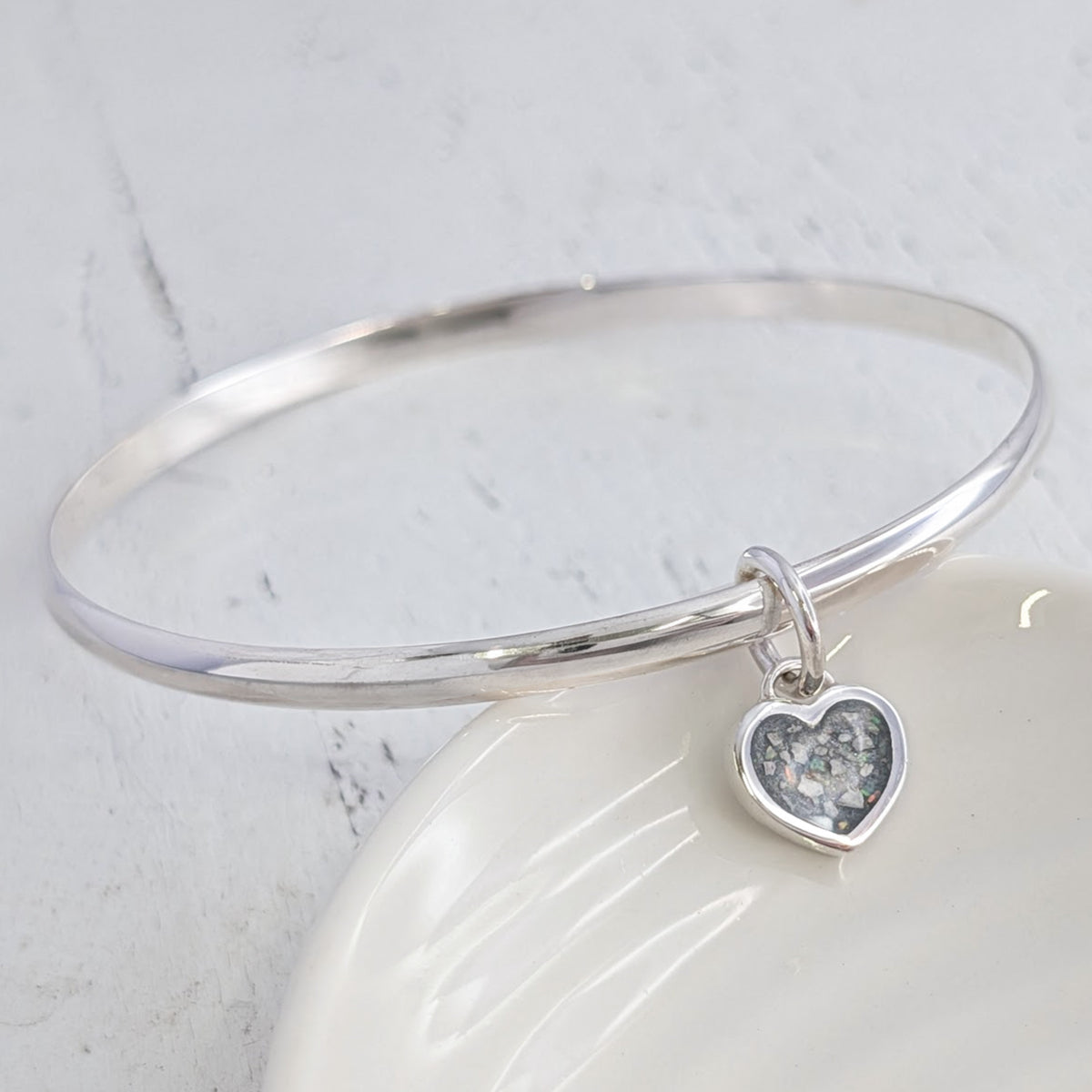 Sterling silver remembrance bangle with heart-shaped ashes charm, individually handcrafted to preserve treasured memories in an elegant and wearable memorial jewellery design.