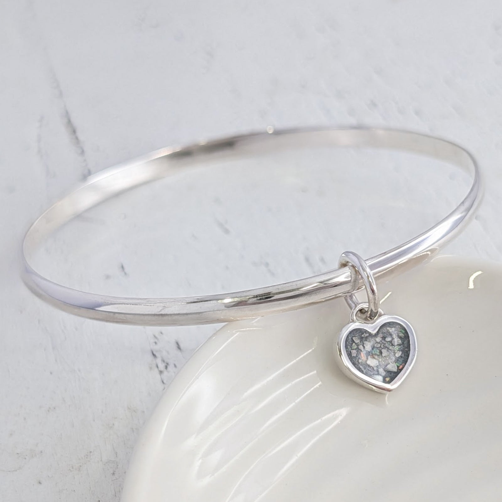 Sterling silver remembrance bangle with heart-shaped ashes charm, individually handcrafted to preserve treasured memories in an elegant and wearable memorial jewellery design.
