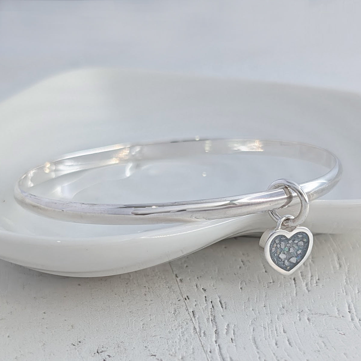Memorial ashes heart charm bangle handcrafted in sterling silver, featuring a delicate heart charm filled with cremation ashes and opal inclusions, creating a meaningful remembrance jewellery piece.