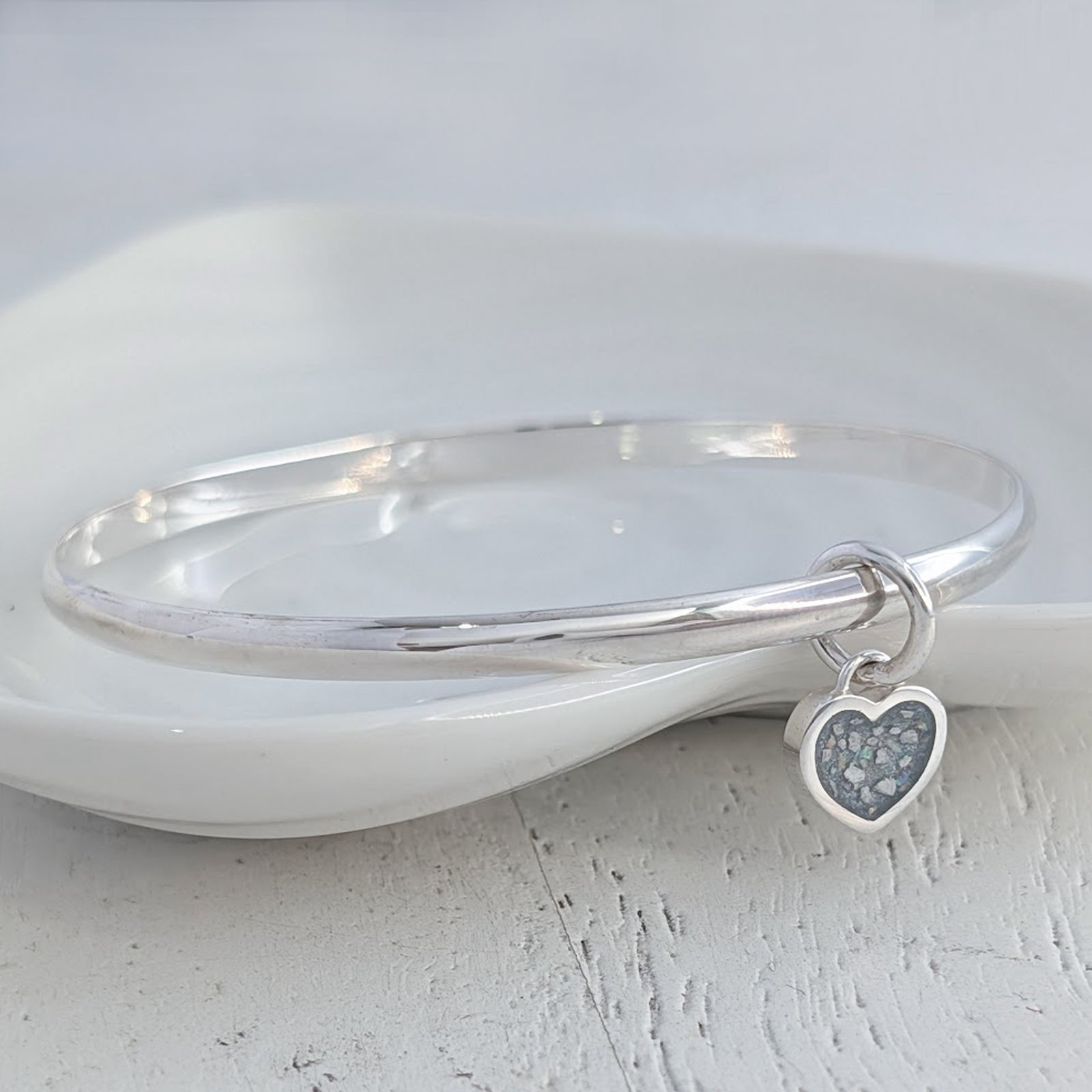 Memorial ashes heart charm bangle handcrafted in sterling silver, featuring a delicate heart charm filled with cremation ashes and opal inclusions, creating a meaningful remembrance jewellery piece.
