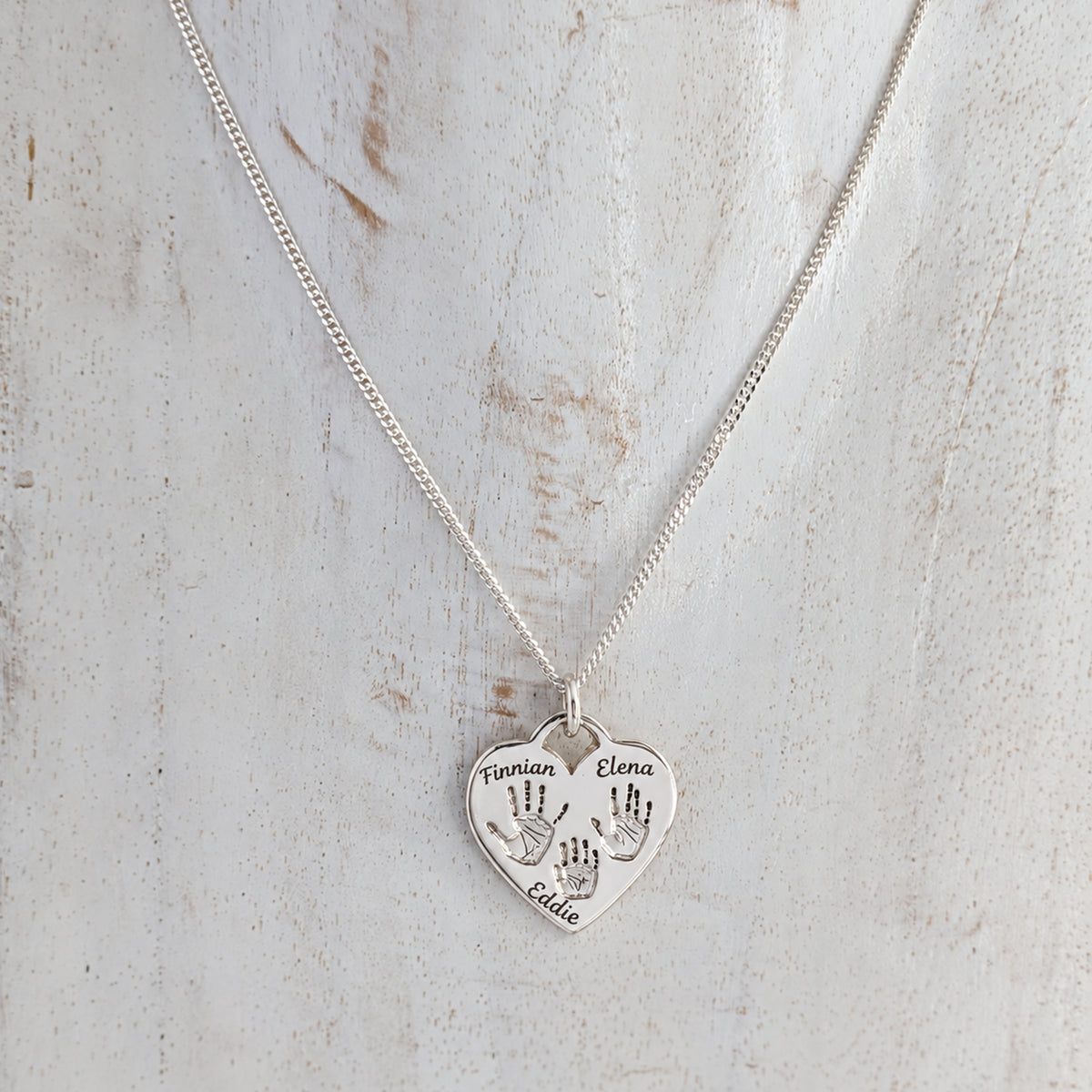 Silver heart shaped pendant engraved with family handprints