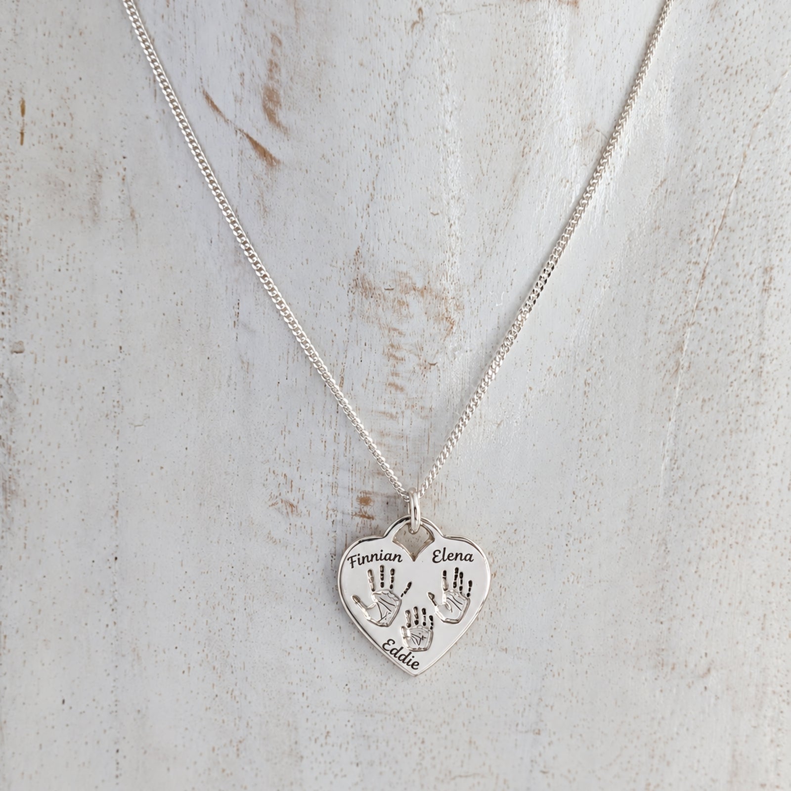 Silver heart shaped pendant engraved with family handprints