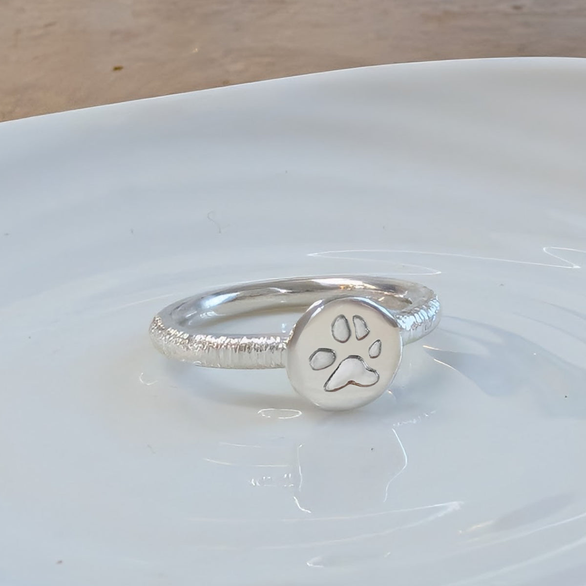 Handmade sterling silver paw print ring with a textured band, personalised pet memorial jewellery featuring an engraved pawprint detail inspired by your beloved dog or cat.