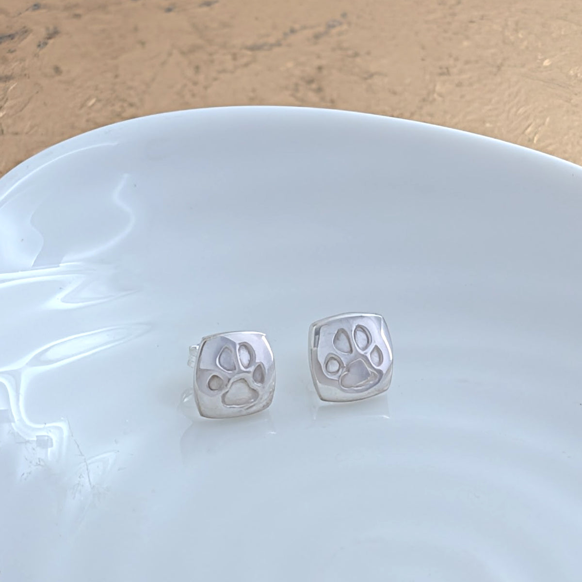 Custom pawprint stud earrings crafted from sterling silver, featuring real pet paw prints engraved onto contemporary cushion-shaped studs. Thoughtful pet remembrance jewellery handmade in Shropshire.